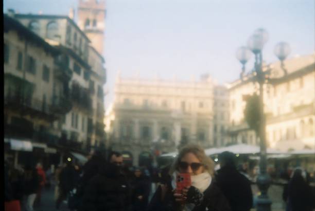 A soft-focused analog film photograph capturing everyday life in a historic European city square. Reflections and motion blur create a nostalgic atmosphere, highlighting people moving through an urban public space. Shot on film, this image evokes timeless street photography, travel, family moments, and authentic city life