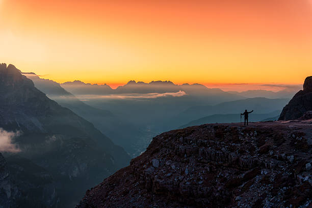 Achievement silhouette hiker standing on rocky summit during golden sunrise with alpine mountain landscape in Dolomites, Italy