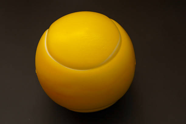 ​A bright yellow tennis ball is centered on a deep dark background, creating a pronounced color contrast.