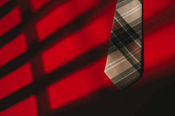 Plaid necktie hanging with dramatic red and black shadow pattern creating bold and stylish contrast in background.