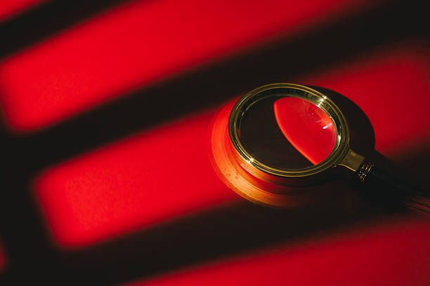 Search concept. Magnifying glass on red surface with dramatic shadows creating mysterious and intense atmosphere in image.