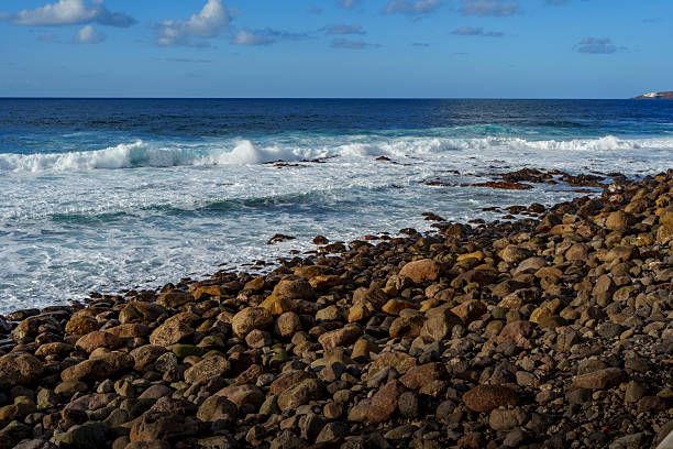 White surf rolls onto a boulder-strewn beach, filling the foreground with texture.
