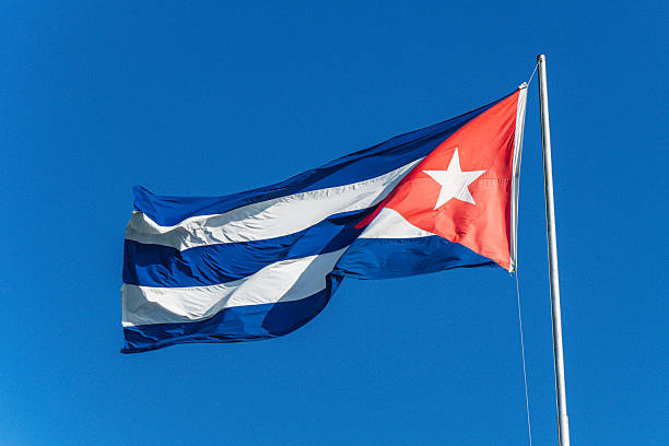 Bright Cuban flag unfurls on a tall pole against a vivid blue sky. This scene evokes national pride, freedom, and outdoor symbolism, captured in Santiago de Cuba, Cuba.