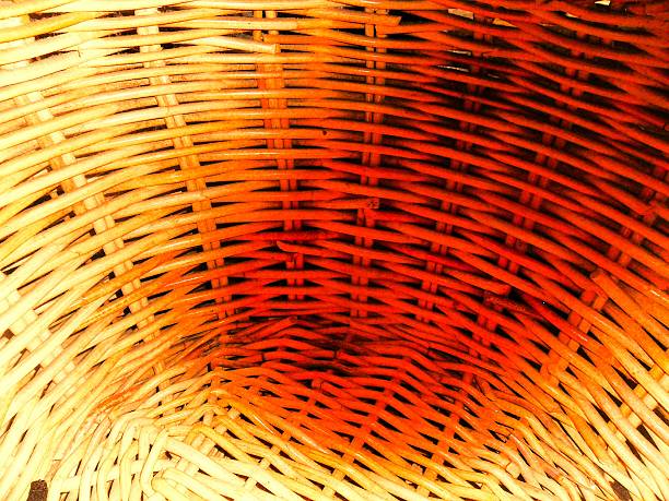 A close-up shot capturing the handcrafted weaving of wicker baskets. The image highlights the intricate weave of natural fibers in warm hues of ochre and golden brown, highlighting the strength and texture of the wood. The strong contrast between light and shadow accentuates the depth and geometry of the overlapping curved lines.