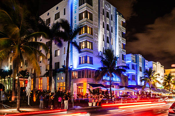 Miami Beach, Florida, United States. July 20, 2009. Vibrant nightlife scene on Ocean Drive featuring illuminated Art Deco hotels, palm trees, outdoor restaurants, and motion blur from passing traffic.