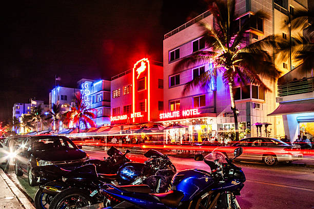 Miami Beach, Florida, United States. July 20, 2009. Nighttime street scene on Ocean Drive featuring the illuminated Boulevard Hotel and Starlite Hotel with neon lights, palm trees, parked motorcycles in the foreground, and long exposure light trails from passing traffic.