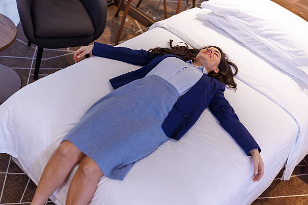 Businesswoman lying on a bed in a hotel room, arms outstretched, resting after a busy day