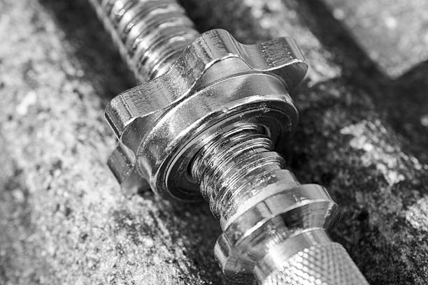 A metal bolt and nut resting on a weathered concrete surface. The shiny hardware contrasts with the gritty background, highlighting industrial hardware, construction, and mechanical precision.
