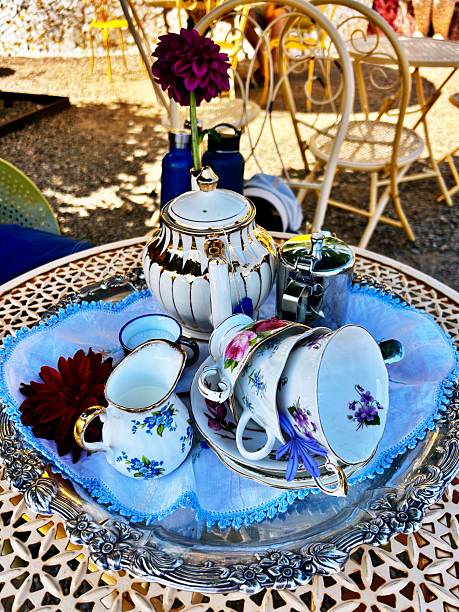 Still life with a beautiful fine porcelain teacup, tea accessories and a pink blossoming branch in an elegant porcelain teapot on a white background