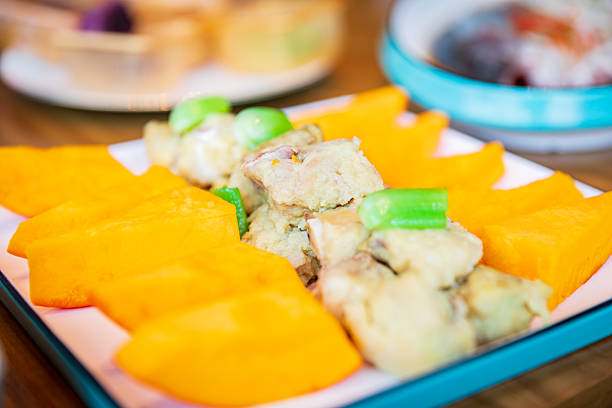 A vibrant dish featuring tender steamed pork with rice flour arranged in the center, flanked by bright orange pumpkin wedges and garnished with green peas for a balanced look.