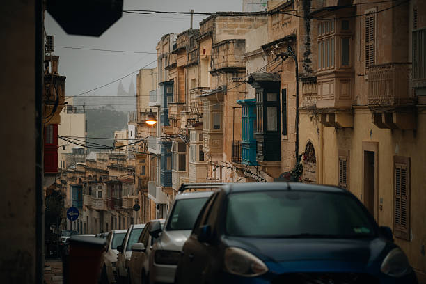Authentic street scene in Sliema, Malta, showcasing traditional Maltese architecture and narrow sidewalks on a rainy day.