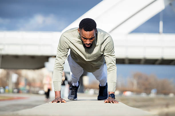 Dedicated young adult man strengthening his body, performing push-ups on a concrete barrier in an urban area, focusing on fitness and a healthy lifestyle