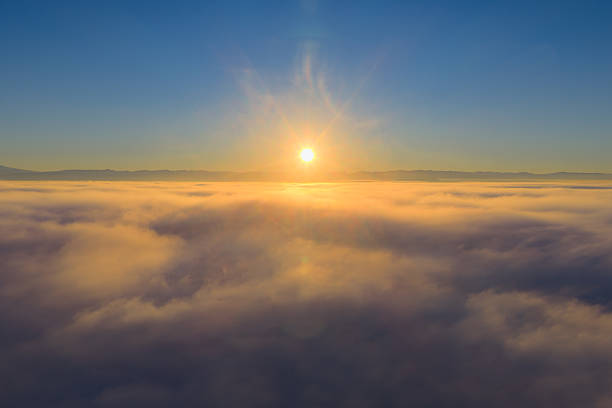 Minimalist view of the sun rising through dense morning fog above a forest, casting a soft orange glow across the sky.