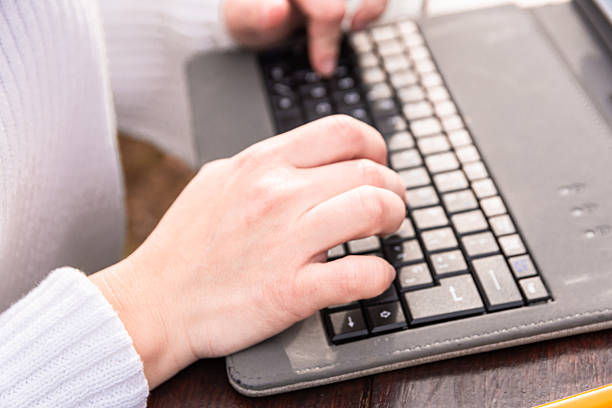 Young woman student typing on a laptop keyboard, focusing on her hands and the technology for education, homework, and online learning in a close up view