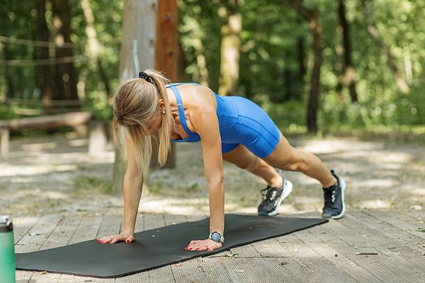 Athletic young woman in blue activewear holding a high plank position on mat during strength training outdoors in the forest.