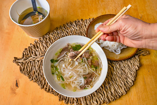Soup Pho Bo. hand with chopsticks, bamboo pad and bowl.