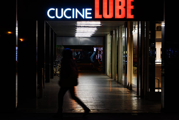 Parma, Italy, January 12 2026: A pedestrian moves through a covered commercial walkway at night with artificial lighting and parked two-wheelers.