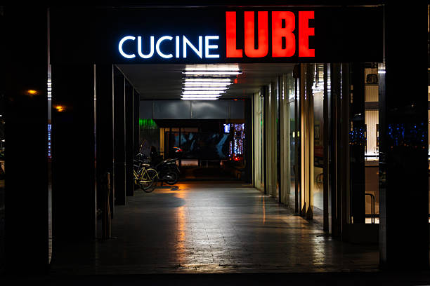 Parma, Italy, January 12 2026: A kitchen furniture store is seen at night with illuminated signage, glass walls, and parked bicycles and a scooter in the background.