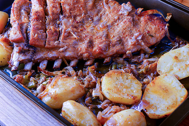 Grilled ribs, baked potatoes and vegetables on wooden background