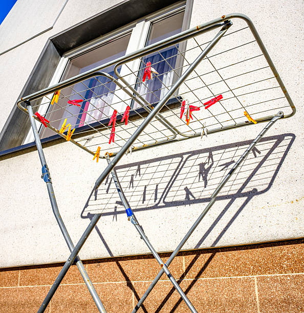 A clothes drying rack is placed outside a wall. Clothespins hold various items as sunlight shines on them during the day.