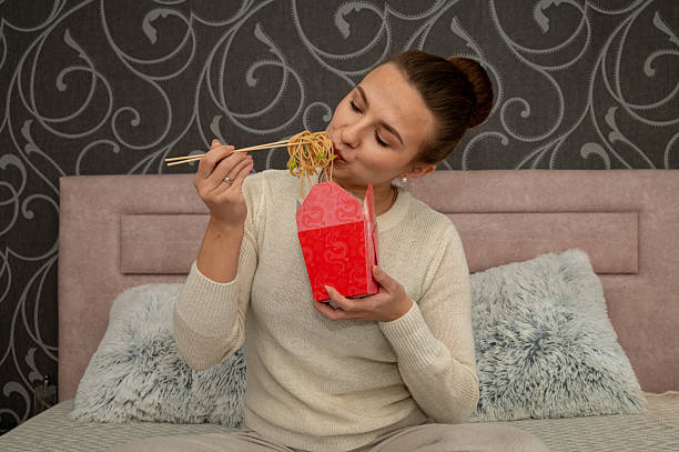 While eating the takeaway food she enjoys. He eats it with chopsticks .