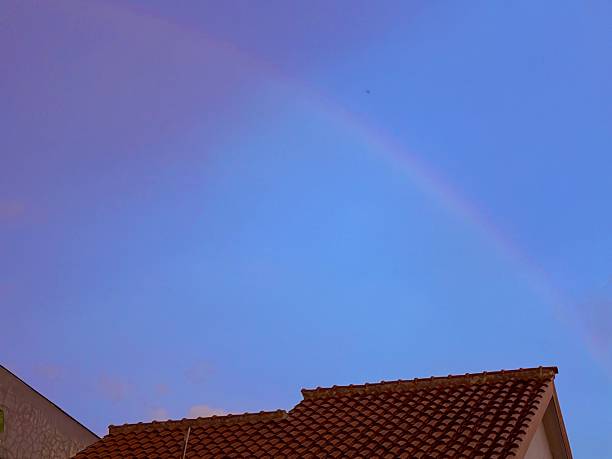 Stock photo of a little girl (8-9) who is pointing out to a rainbow. She is standing in front of house entrance and wears winter clothing.