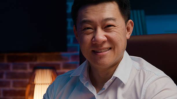 Portrait smiling Asian business man looking at camera working posing in evening office cheerful Korean businessman work smile headshot Japanese Chinese male specialist professional at night workplace. High quality photo