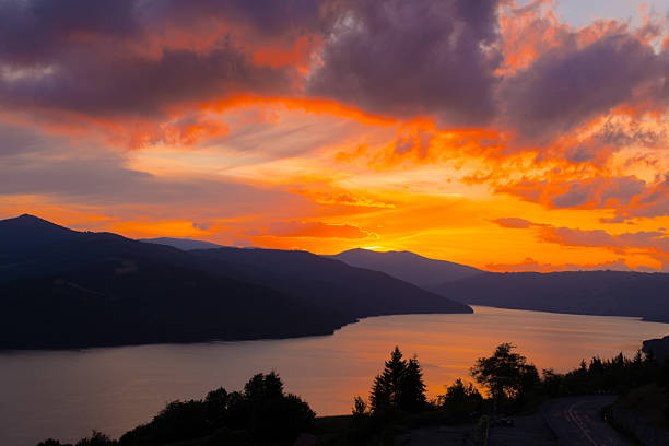 Vibrant sunset colors reflect on the calm lake surrounded by mountains. Nature showcases its beauty as day transitions to night in this scenic landscape.