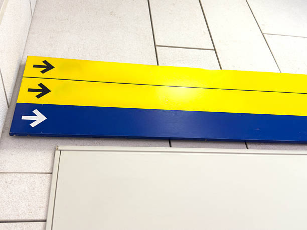 Photo captures a close-up of the number two encircled in blue on a concrete surface. Surrounding the number are grey, grooved lines, and a row of contrasting yellow tactile tiles positioned at the bottom of the frame.