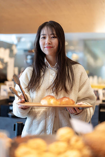 Female high school student choosing bread in bakery - looking at camera