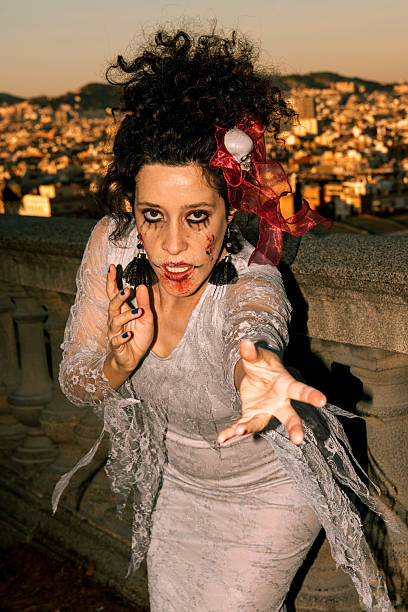 Woman portraying a spooky witch character during a carnival or halloween event, featuring dramatic makeup with blood and dark eyes, curly hair, and an outstretched hand reaching towards the viewer