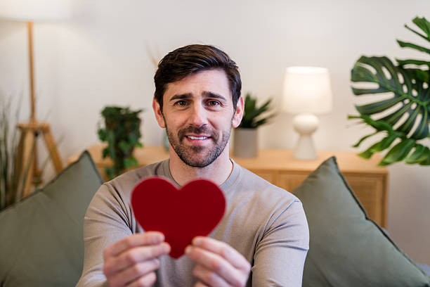 Man smiling while holding a red heart shape, symbolizing love and care