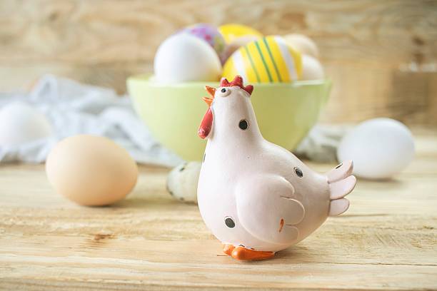 Easter chicken figurine with decorated and natural eggs on wooden background. Rustic still life with fresh farm eggs and decorative chicken figurine.