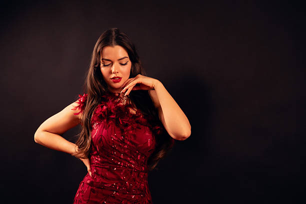 A woman in a red dress stands with a relaxed posture and a thoughtful look on her face. She appears to enjoy a special moment for Valentines Day.