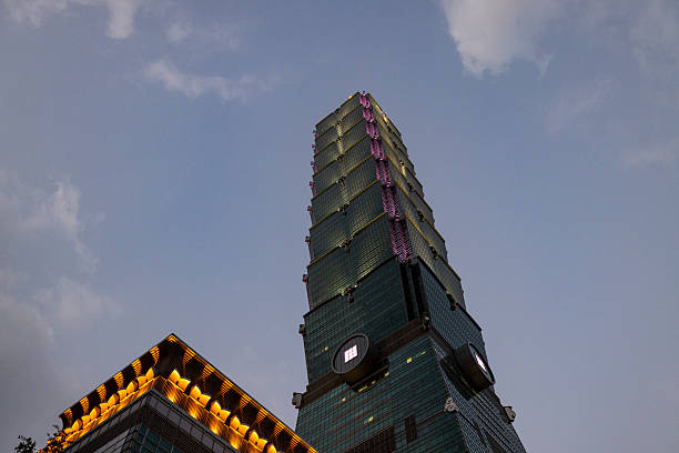 Low-angle dusk view of Taipei 101 in Taipei, Taiwan. The iconic tiered skyscraper is partially illuminated against a twilight sky, highlighting modern Asian architecture and urban nightlife in the city center.