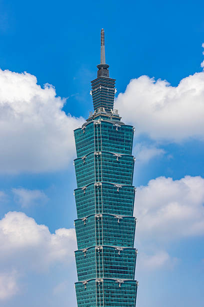 Close-up view of Taipei 101 rising above Taipei, Taiwan. The iconic tiered skyscraper is shown against a bright blue sky with scattered clouds, highlighting modern Asian architecture and urban landmarks in daylight.