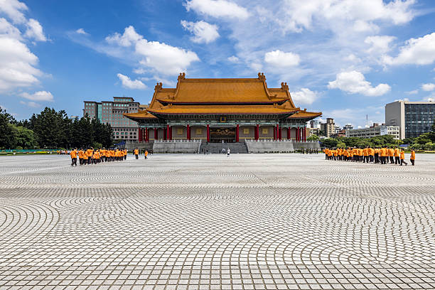 Symmetrical view of the National Concert Hall in Taipei, Taiwan, featuring traditional Chinese architecture with a golden tiled roof and a wide public plaza. Organized groups of visitors gather in front of the building, illustrating civic space, cultural tourism, and public life at Liberty Square in daylight.