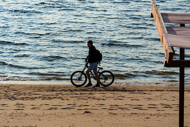 Samara, Russia - June 3, 2025: a cyclist walks along the beach along the shore