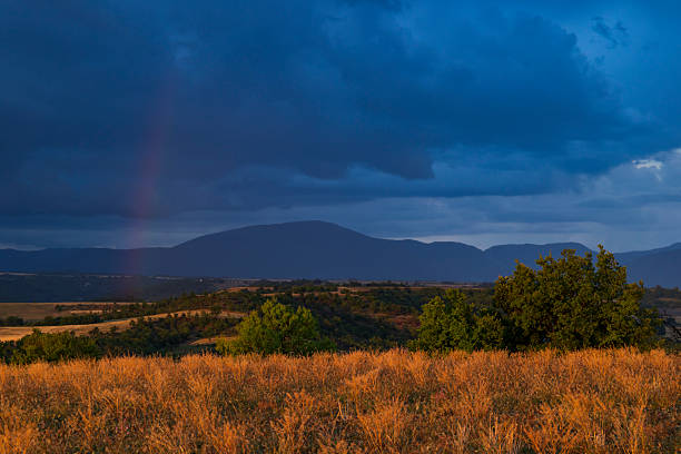 Sunset illuminating dry grass field under dark stormy sky with light ray in Entrevennes, France