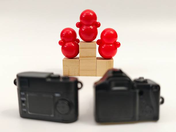 Three plastic dolls figures are staged on blocks, photographed by two cameras represent celebration or achievement ceremony scenario.