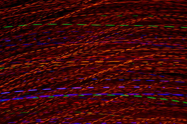 Bright light trails and spots create futuristic patterns against a dark backdrop. Abstract background with defocused lines and spots, made by glowing fiber optic lights.