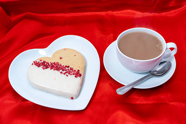 Heart shaped cookie biscuit with a hot drink on a red satin background