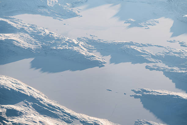 Aerial view from an airplane window showing snow-covered mountains and ice in greenland