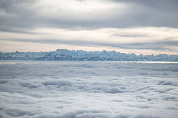Snow-capped alps mountain range rising above a vast sea of clouds from an airplane view