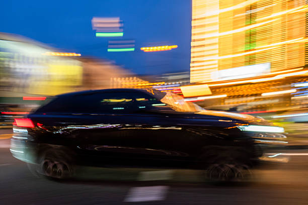 Urban life at night with a speeding dark car on a street, creating dynamic motion blur against illuminated buildings