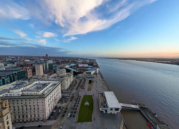 An aerial image captured over the Liverpool waterfront, showing parts of the city including the historic Liverpool docks and the River Mersey. The scene is photographed at sunset, with warm light reflecting across the water and surrounding urban landscape. Suitable for editorial, travel, and cityscape use.