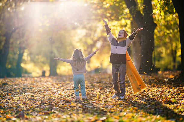 Two cheerful children throwing autumn leaves into the air, celebrating fall season.