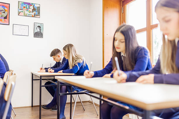A group of high school students concentrating on their exams in a bright classroom.