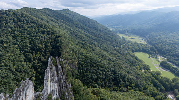 Wide aerial shot of a sharp vertical rock fin rising above a lush green mountain valley.