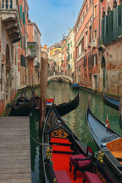 Several gondolas are moored along a narrow canal between old buildings in Venice, Italy, with a small pedestrian bridge in the distance